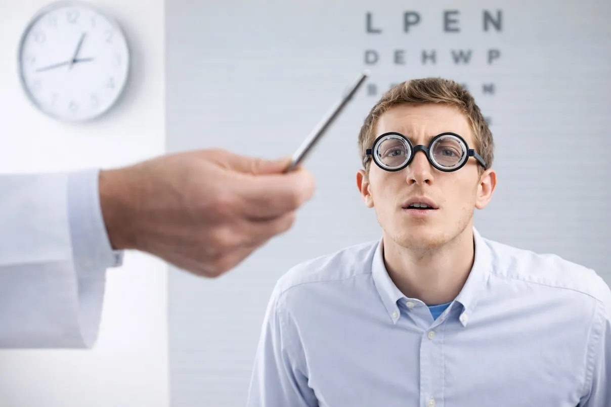 Giovane uomo ipovedente durante una visita optometrica che segue con lo sguardo una penna, indossando lenti di prova.