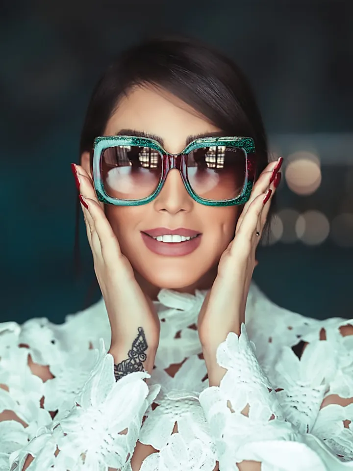 Donna che indossa occhiali da sole alla moda con montatura verde, in posa frontale su sfondo sfocato.