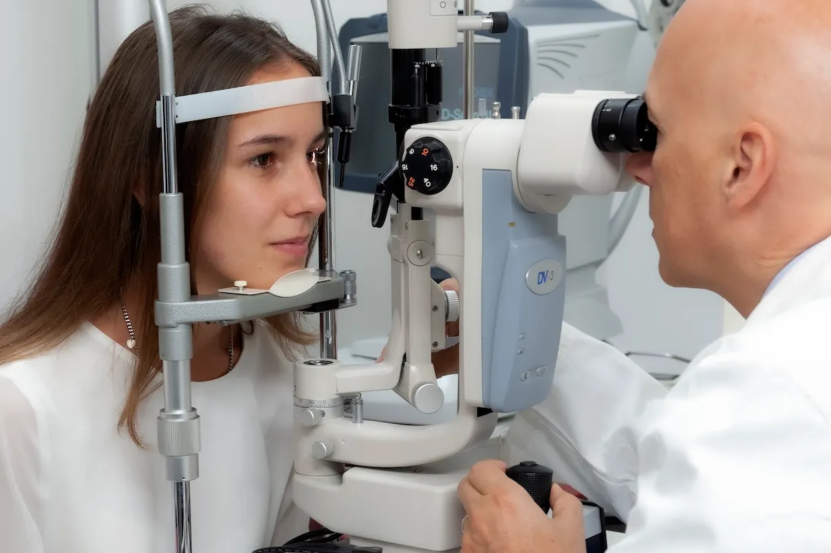 Ragazza sottoposta a visita optometrica con lampada a fessura mentre l’optometrista osserva l’occhio attraverso lo strumento in ambulatorio.